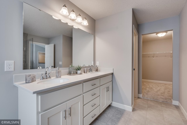 full bath with a walk in closet, double vanity, tile patterned flooring, baseboards, and a textured ceiling