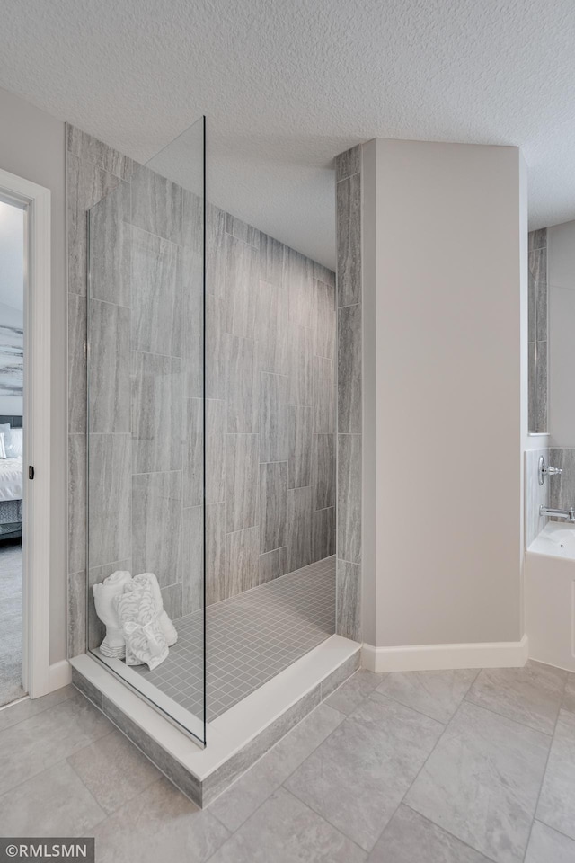 ensuite bathroom with a walk in shower, a textured ceiling, a bath, marble look tiles, and baseboards