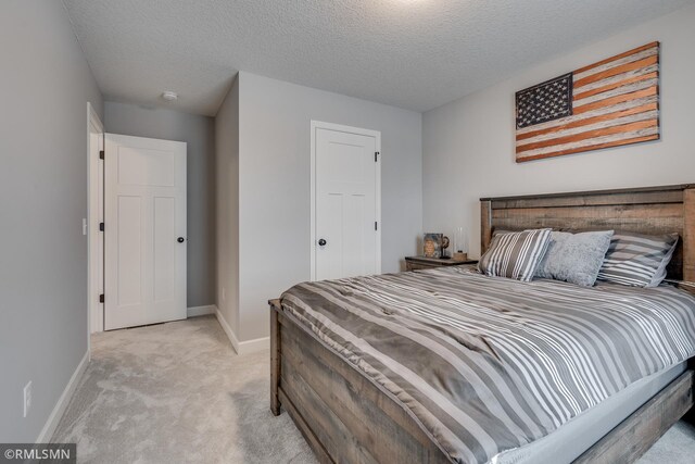 bedroom with light colored carpet, baseboards, and a textured ceiling