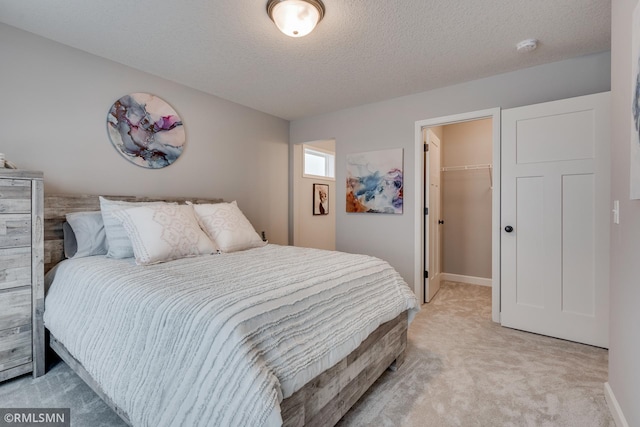 bedroom featuring light colored carpet, a textured ceiling, a spacious closet, a closet, and baseboards