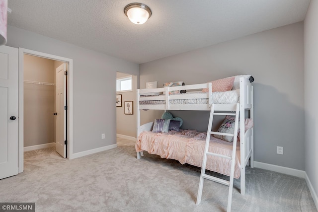 bedroom with carpet, baseboards, a textured ceiling, and a walk in closet