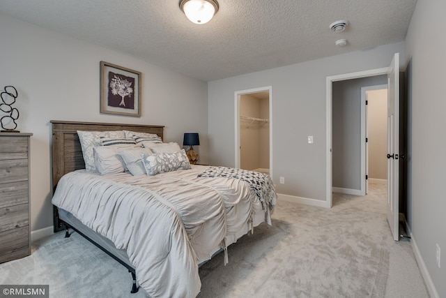 bedroom featuring light carpet, a textured ceiling, a spacious closet, a closet, and baseboards