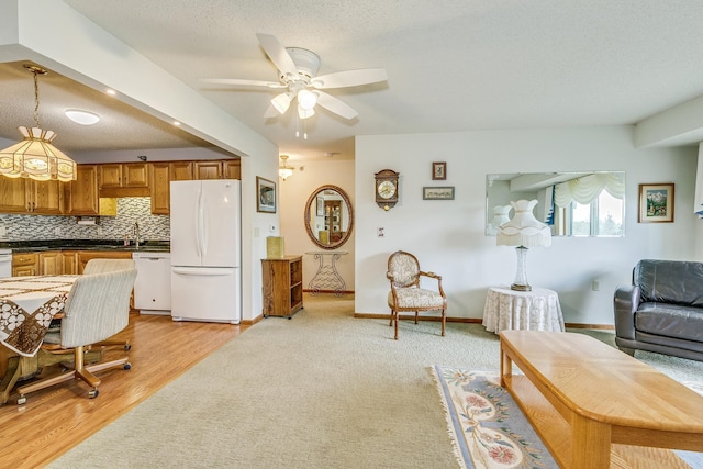 living area featuring a ceiling fan, baseboards, light wood-style flooring, light colored carpet, and a textured ceiling