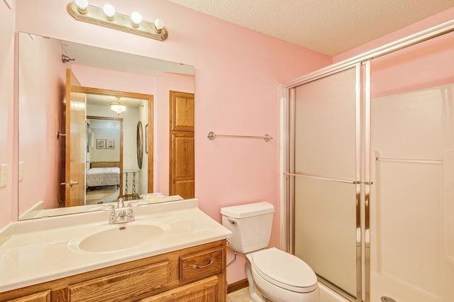 ensuite bathroom featuring a shower stall, toilet, vanity, and a textured ceiling