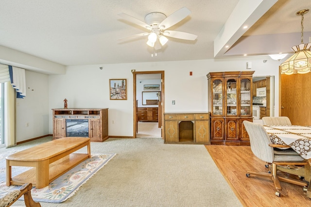 living room featuring ceiling fan, a fireplace, baseboards, and light colored carpet