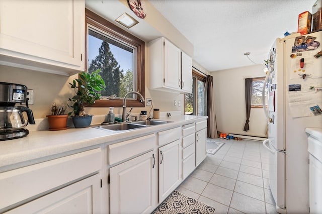 kitchen with freestanding refrigerator, a sink, light tile patterned floors, light countertops, and white cabinets