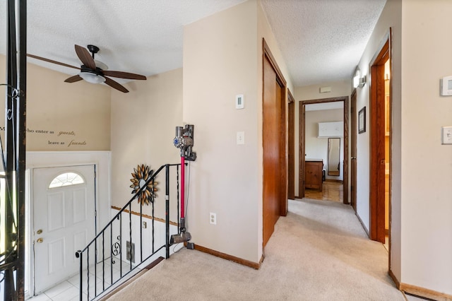 foyer entrance featuring a textured ceiling, ceiling fan, light carpet, and baseboards