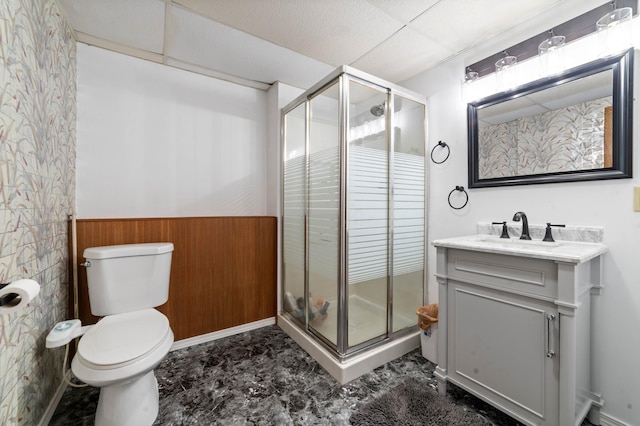 full bath featuring a wainscoted wall, a shower stall, toilet, vanity, and a paneled ceiling