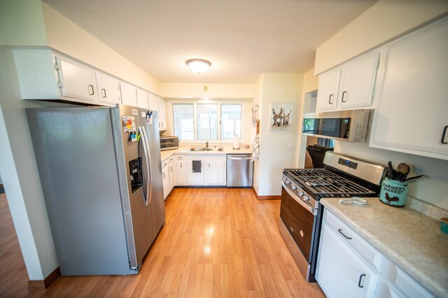 306 Hiawatha Dr E, Wabasha, MN 55981 - kitchen with stainless steel appliances, a sink, light wood-type flooring, white cabinets, and a textured ceiling