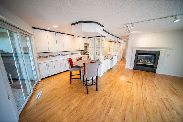 1723 Teton Ln NE, Rochester, MN 55906 - kitchen with white cabinets, light wood-style flooring, stainless steel stove, a tiled fireplace, and a textured ceiling