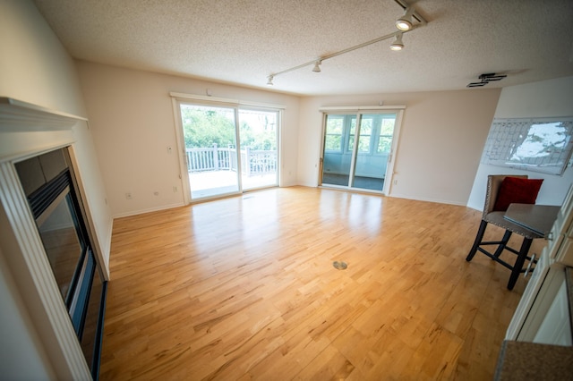 1723 Teton Ln NE, Rochester, MN 55906 - unfurnished living room with track lighting, light wood finished floors, a glass covered fireplace, a textured ceiling, and baseboards