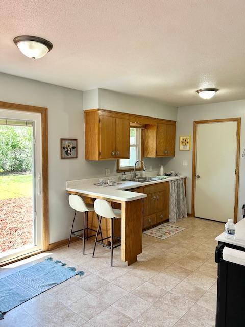 kitchen featuring brown cabinets, a peninsula, light countertops, healthy amount of natural light, and a textured ceiling