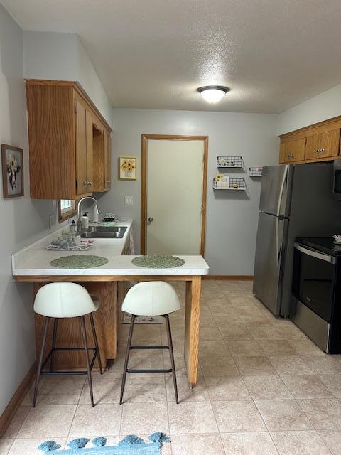 kitchen with stainless steel appliances, a sink, light countertops, a peninsula, and brown cabinetry