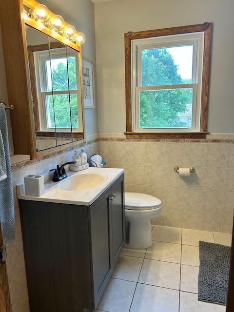 7731 80th St S, Cottage Grove, MN 55016 - bathroom with plenty of natural light, tile patterned floors, tile walls, vanity, and wainscoting