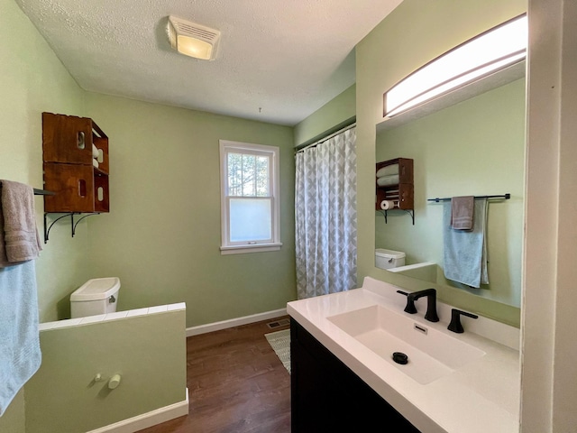 full bathroom with toilet, wood finished floors, vanity, baseboards, and a textured ceiling