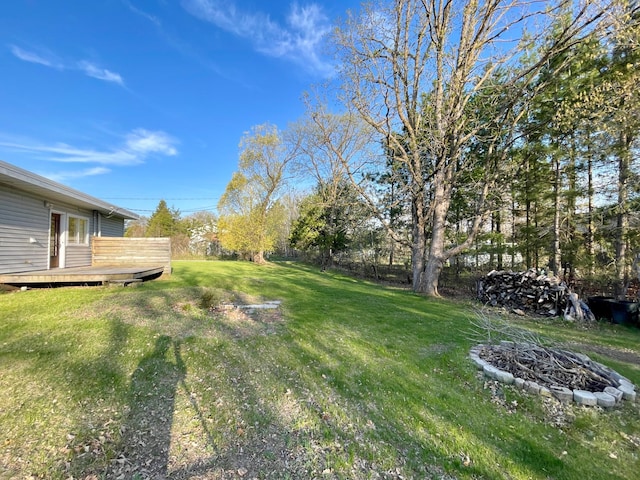 view of green lawn with an outdoor fire pit and a deck