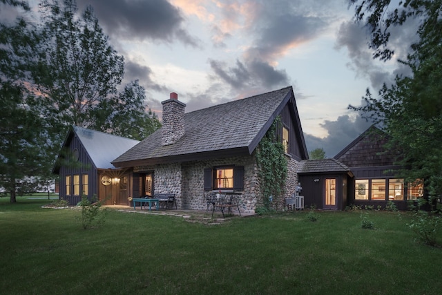119 Lynn Rd, Ottertail, MN 56571 - back of house at dusk with a lawn, a chimney, and stone siding