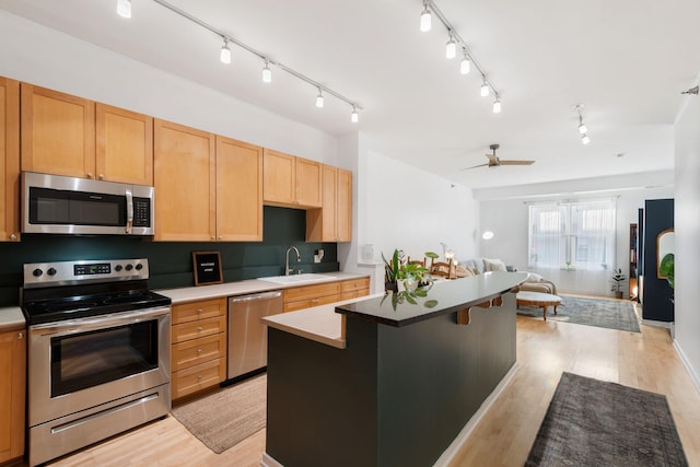 kitchen featuring stainless steel appliances, open floor plan, a sink, light brown cabinetry, and a kitchen island