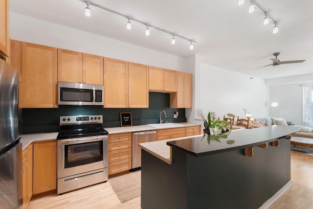 kitchen with appliances with stainless steel finishes, rail lighting, open floor plan, a sink, and light brown cabinetry