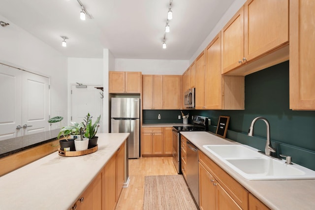 kitchen with stainless steel appliances, a sink, light wood-style flooring, and light brown cabinetry