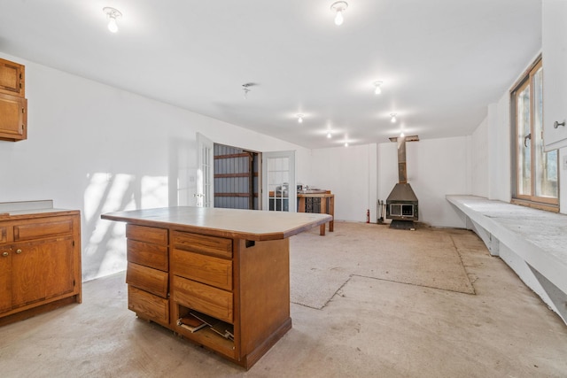 5230 Rebecca Park Trl, Greenfield, MN 55357 - kitchen featuring a wood stove, a center island, brown cabinets, light countertops, and concrete floors