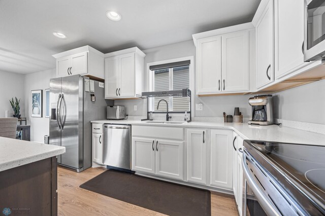 kitchen with stainless steel appliances, a sink, white cabinetry, recessed lighting, and light wood finished floors