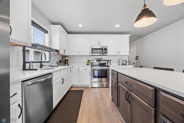 kitchen with stainless steel appliances, a sink, white cabinets, light wood-style floors, and recessed lighting