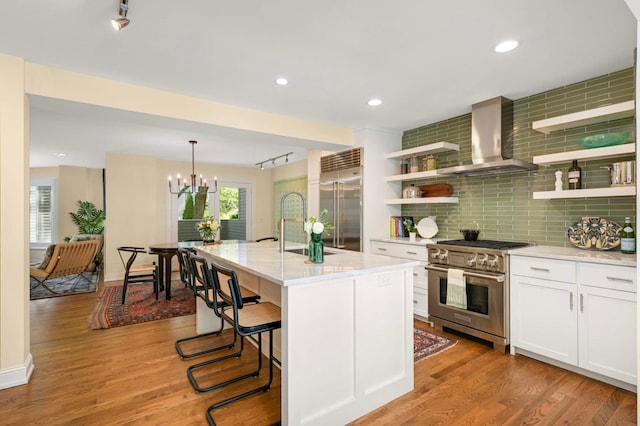 28 Greenway Gables, Minneapolis, MN 55403 - kitchen featuring high quality appliances, wall chimney exhaust hood, open shelves, tasteful backsplash, and wood finished floors