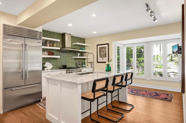 28 Greenway Gables, Minneapolis, MN 55403 - kitchen with stainless steel built in refrigerator, wall chimney range hood, decorative backsplash, light stone counters, and open shelves