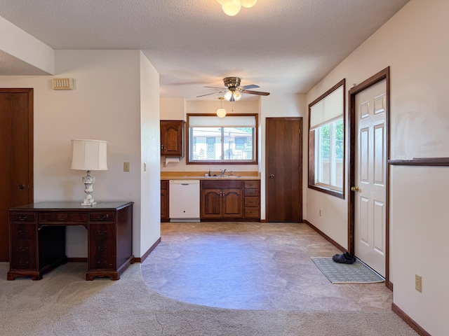 kitchen featuring white dishwasher, light colored carpet, a sink, a ceiling fan, and baseboards