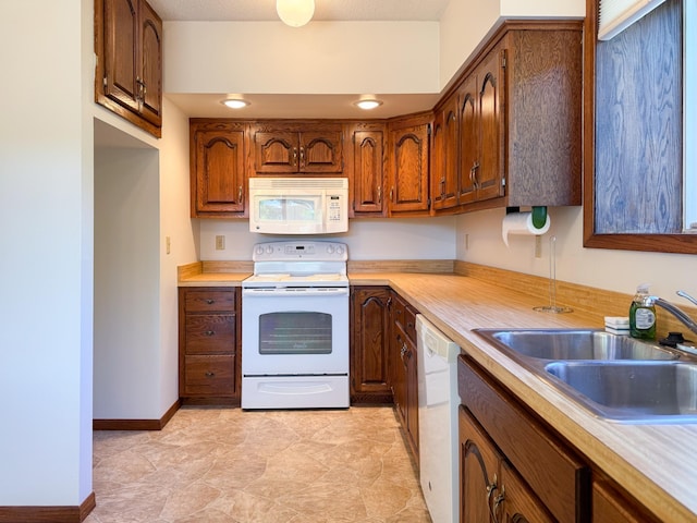 kitchen featuring white appliances, light countertops, a sink, and brown cabinetry