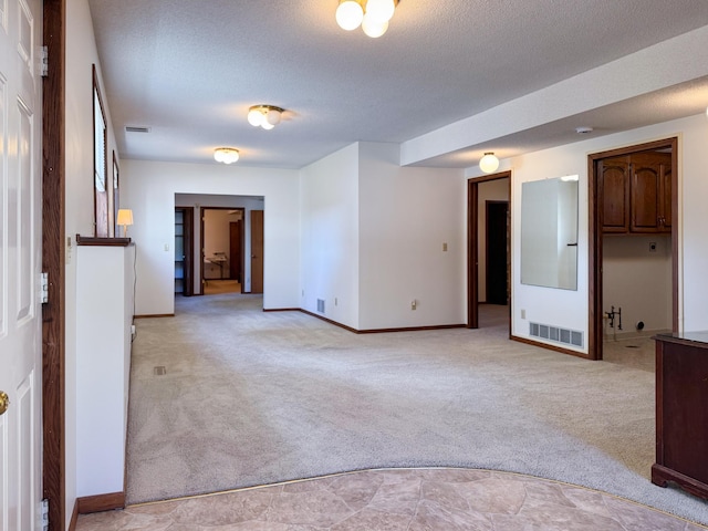 spare room featuring light colored carpet, baseboards, and a textured ceiling