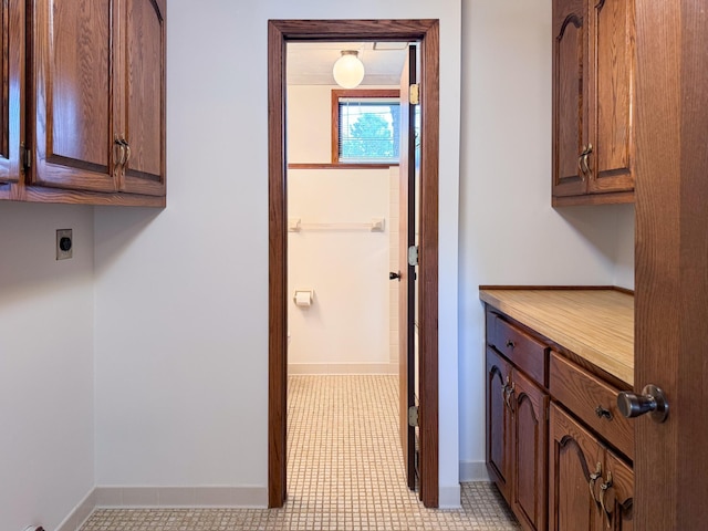 clothes washing area featuring electric dryer hookup, cabinet space, and baseboards