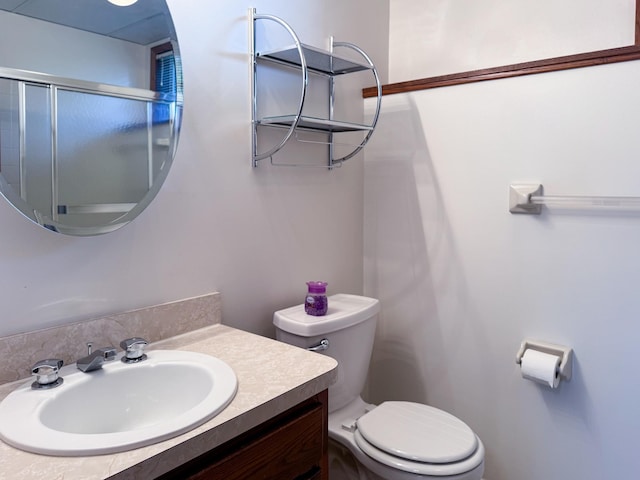 bathroom featuring toilet, vanity, and a shower with shower door