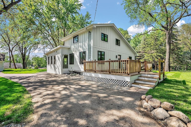 rear view of property featuring board and batten siding, a deck, and a yard