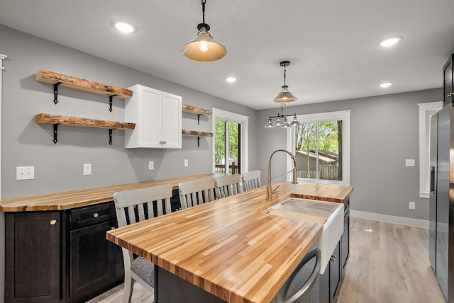 kitchen with wood counters, open shelves, a sink, white cabinetry, and pendant lighting