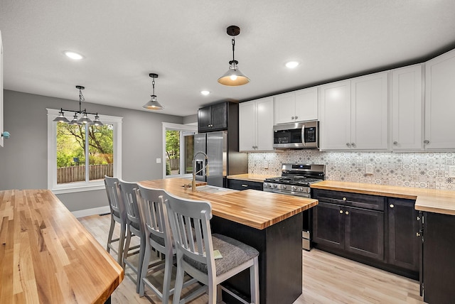 kitchen with wood counters, appliances with stainless steel finishes, light wood-type flooring, decorative backsplash, and recessed lighting