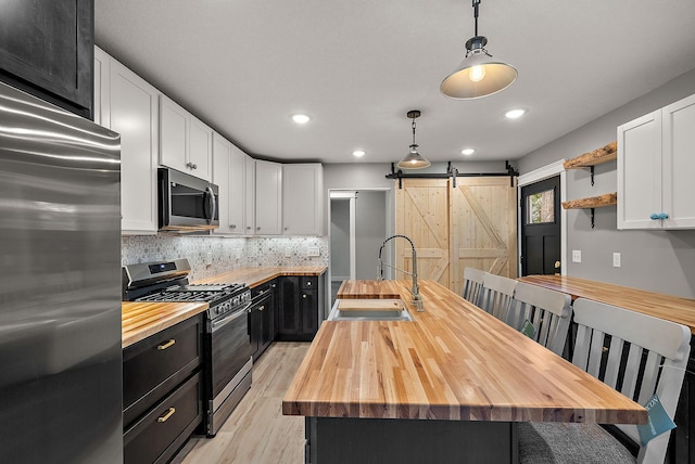 kitchen with wooden counters, stainless steel appliances, a sink, dark cabinets, and a barn door