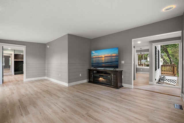 unfurnished living room featuring wood finished floors, baseboards, a wainscoted wall, a glass covered fireplace, and recessed lighting