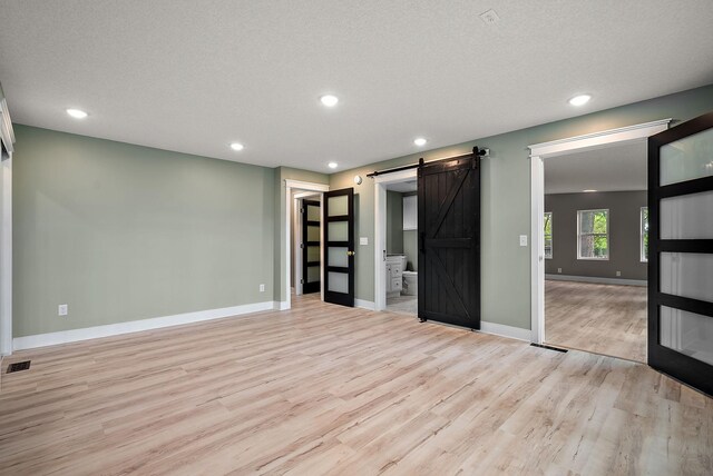unfurnished room featuring a barn door, light wood-type flooring, baseboards, recessed lighting, and a textured ceiling