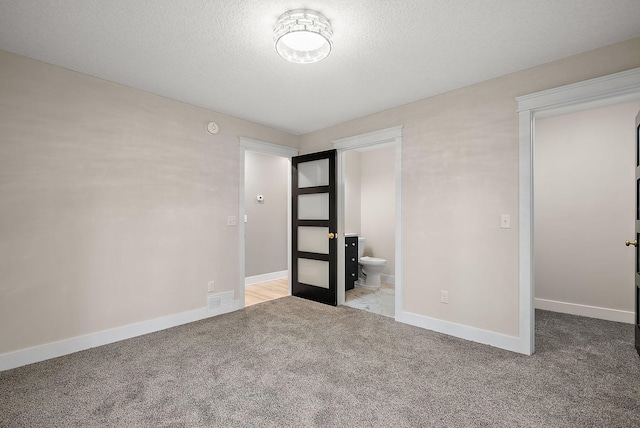 unfurnished bedroom with carpet, baseboards, a textured ceiling, and connected bathroom