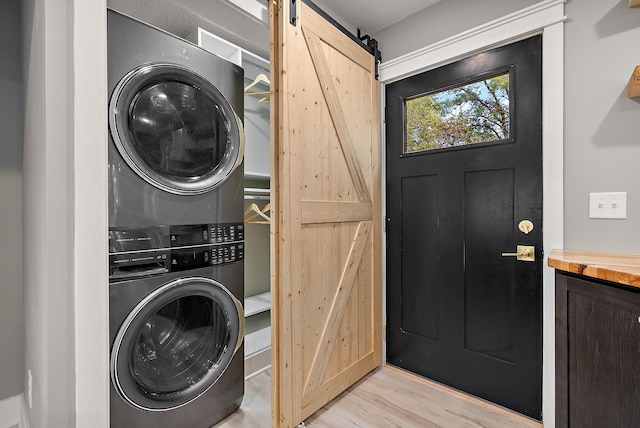 laundry room with stacked washer and clothes dryer, a barn door, and light wood finished floors
