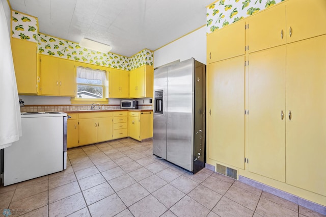 kitchen featuring appliances with stainless steel finishes, yellow cabinetry, a sink, and light tile patterned flooring