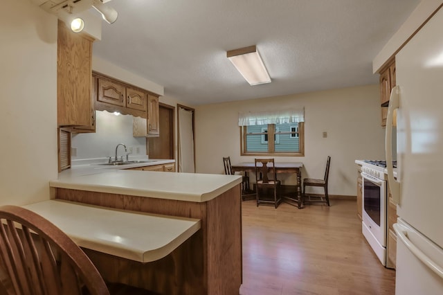 607 Wilson St, Downing, WI 54734 - kitchen with white appliances, a sink, light countertops, light wood-style floors, and a peninsula