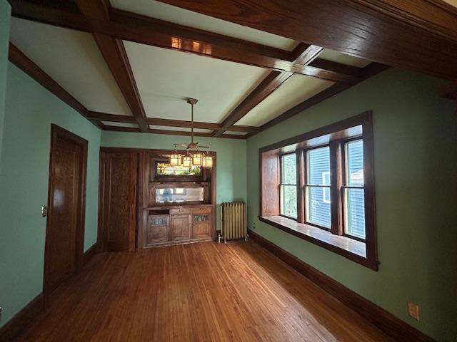unfurnished dining area featuring radiator, a chandelier, baseboards, wood finished floors, and coffered ceiling