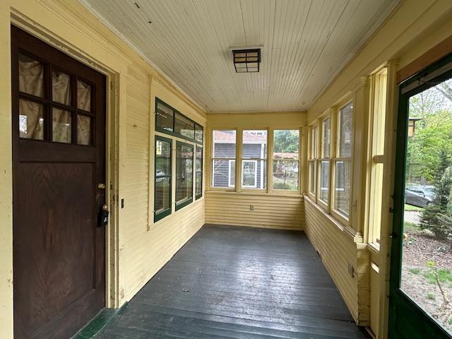 unfurnished sunroom with plenty of natural light, crown molding, wooden ceiling, wooden walls, and wood-type flooring