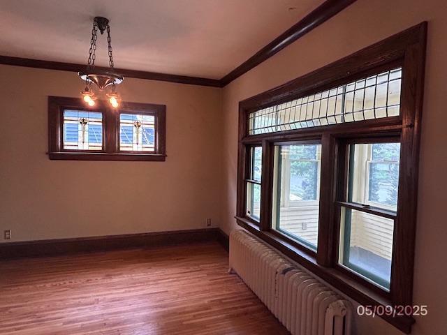empty room with radiator, crown molding, wood finished floors, and baseboards