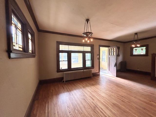 unfurnished living room with radiator heating unit, baseboards, wood finished floors, a chandelier, and ornamental molding