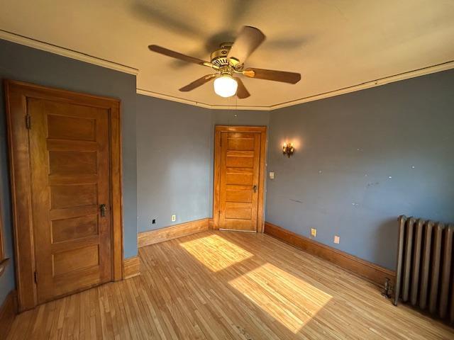 unfurnished room featuring radiator heating unit, wood finished floors, ceiling fan, crown molding, and baseboards