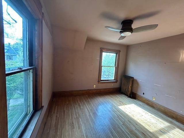 unfurnished room featuring hardwood / wood-style flooring, radiator heating unit, baseboards, and ceiling fan